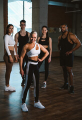 Fototapeta na wymiar Group of happy smiling muscular sports fitness female and male adults people standing together as good friends in gym with sport equipment in background after a difficult workout session