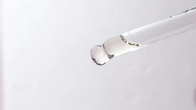 Close-up of a glass pipette with a cosmetic product for body skin care on a light gray background.