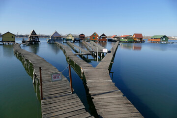 Fototapeta premium Colorful fishing cabins connected to a lake by narrow wooden piers by lake Bokod near Oroszlany, Hungary. It is also called the floating village. (no entry signs)