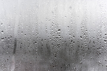 Steamy window with water drops made in dull day, condensation on glass with drops flowing down, humidity and foggy blank