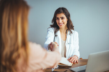 Smiling young Caucasian female doctor shake hand greeting get acquainted with female patient in...