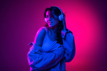 Beautiful young emotional girl, student with long dark hair isolated on gradient pink-blue background in neon light. Concept of emotions, youth