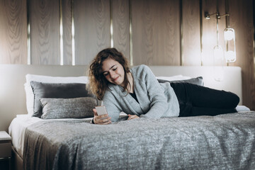 Obraz premium Happy laughing teenager girl watching video on phone. Online chat with friends. Girl lying on bed