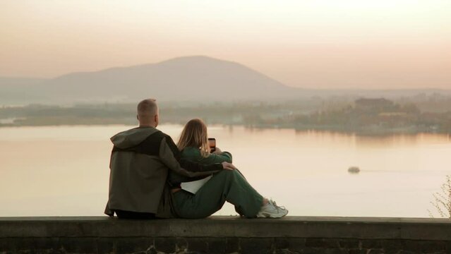 Lovely young couple watching the sunset in the evening in Sevan lake, Armenia. Enjoying beautiful and paceful sunset