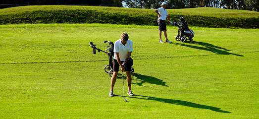 Golfer on a golf course in the summer on a sunny day, hitting the ball with a golf club.