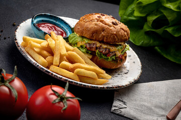 burger with fried steak vegetables and cheese, served with french fries and sauce, on a dark background
