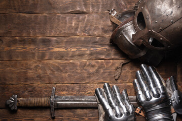 Medieval concept background. Knight helmet, iron gloves and sword on the wooden table flat lay...