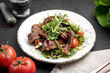 salad of steak, arugula and cherry tomatoes, on a dark background