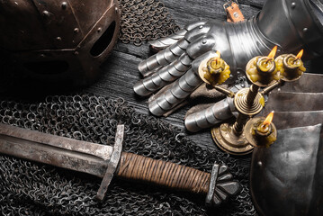 Knight sword, helm and chain mail armor on the black wooden table background close up.