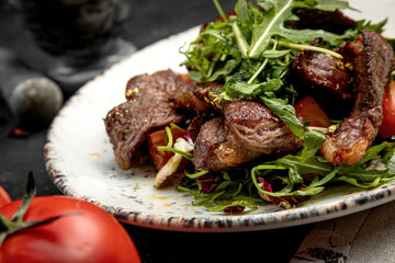 salad of steak, arugula and cherry tomatoes, on a dark background