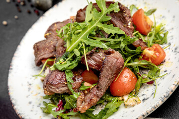 salad of steak, arugula and cherry tomatoes, on a dark background