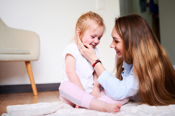 Happy family. Young mom hugs her cute little daughter at home while lying on the floor