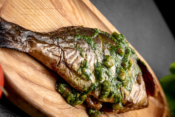 grilled fish served with lemon on a wooden board, on a dark background