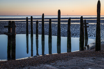 Sunset and reflections of groynes at Rye Harbour, East Sussex, England