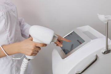 A woman tunes a laser hair removal machine. Girl holding a working part of the epilator in her hands in a modern beauty salon. Underarm Laser Hair Removal concept