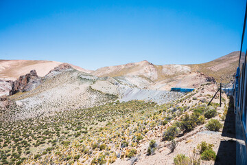 Blue train riding through desert mountains. Clear sky. Horizontal. With copy space.