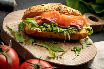 sandwich with salmon and arugula served on a wooden board on a dark background