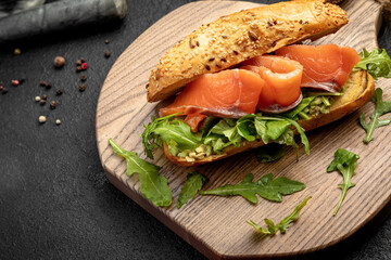 sandwich with salmon and arugula served on a wooden board on a dark background