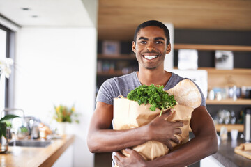 Im ready to impress my lady tonight. Shot of a young african man holding a bag of groceries indoors.