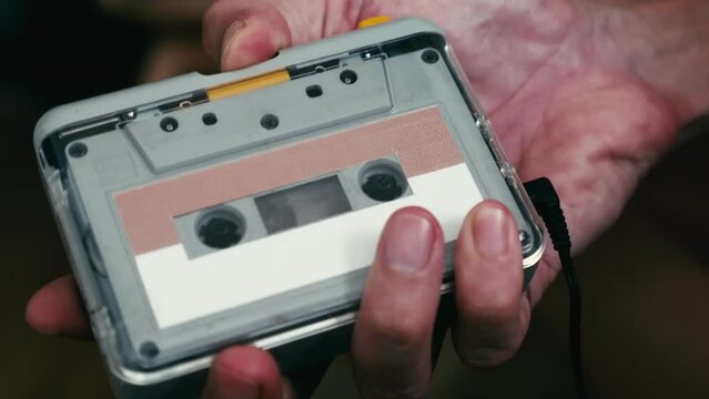 Close up of a man's hand inserting a cassette tape into a cassette player. 