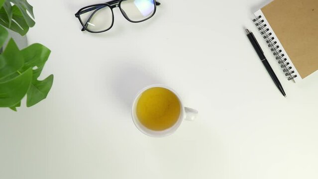 Put a cup of tea on the desktop in the office. Top view of green tea in a white mug. Break at work. Glasses and notebook in the office. Meditation for recuperation.