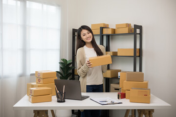 Beautiful young asian entrepreneur standing pose smiling to camera. Female small Business owner with box working at home. Startup freelance people with many parcel on background.