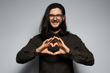 Portrait of young smiling man with long hair, gesturing heart sign with hands.
