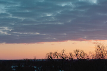 Obraz premium A full frame cloudy sky with little holes showing blue sky. Silhouette of trees in the bottom of a frame