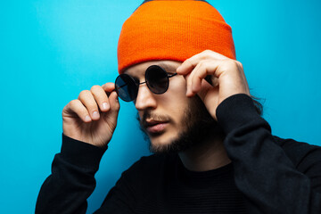 Serious man on blue background. Wearing round sunglasses and orange hat.