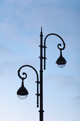 A double black street lamp with two (2) light bulbs against cloudy blue sky