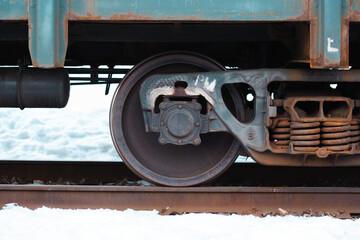 Fototapeta na wymiar A closeup of a steel wheel of a train on the rail during a snowy winter. Rusty springs on the right side of the frame.
