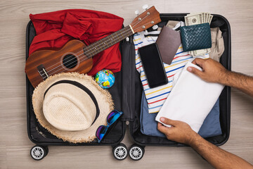 Top view Close up male hands organize luggage. Put clothes and pants in trolley bag and prepare to go abroad. Preparing suitcase for summer vacation trip. Traveler accessories open luggage.