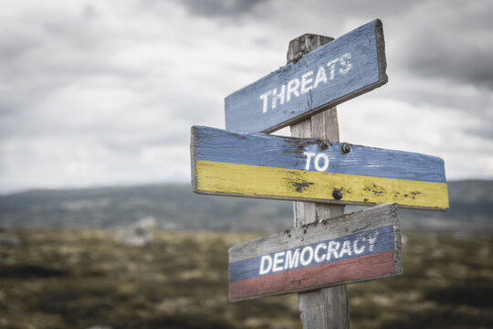 threaths to democracy text quote on wooden signpost outdoors on nato colored flag, ukrainian flag and russian flag.