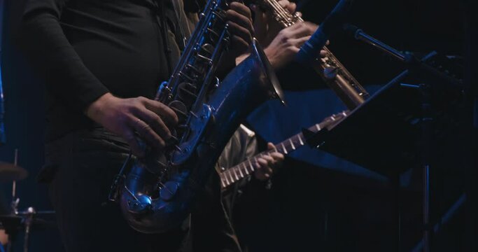 Man saxophonist at a concert plays the saxophone and dances. Live musical performance and virtuosity of playing a brass musical instrument. It dark, colored spotlights are shining around