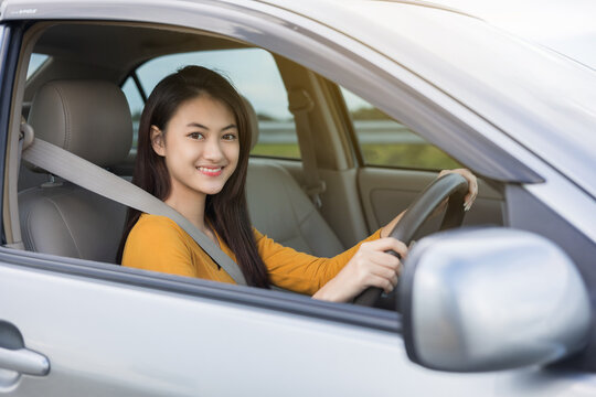 Young beautiful asian women getting new car. she very happy and excited looking outside window. Smiling female driving vehicle on the road on a bright day