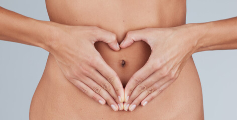 Giving some love to my gut. Cropped shot of an unrecognizable woman standing alone in the studio and making a heart-shaped gesture over her tummy.