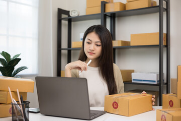 Young asian entrepreneur woman checking product on stock take note with laptop. Business woman working SME online at home. Check address on parcel. Small business owner start up freelance concept.