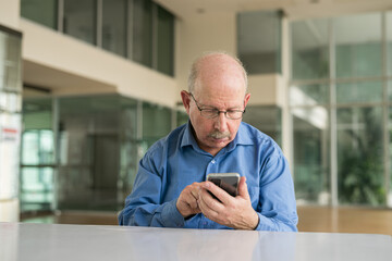 Portrait of senior businessman sitting at office and using phone