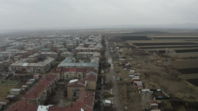 Aerial view buildings in city, near cultivated lands. Drone fly over buildings, road, 
cottage houses in Gyumri, Armenia.