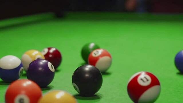 Closeup of billiard balls on table assembled in triangle, formation breaks white ball that was hit with cue. Man is playing billiards. Entertainment concept
