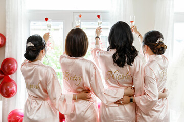 Bridesmaids and bride in pink robes standing with their backs to the camera holding champagne...