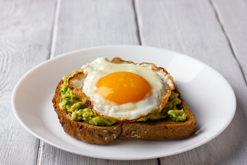 Avocado toast with fried egg on white wooden background. Tasty healthy breakfast.