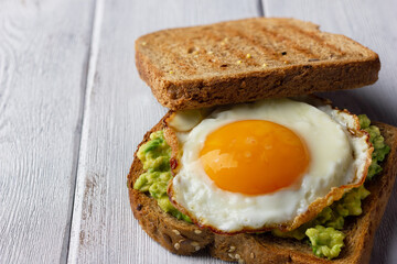 Avocado toast and fried egg with whole grain bread on white wooden background for healthy breakfast.