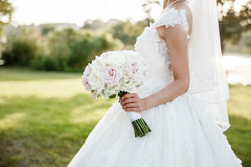 Beautiful white wedding bouquet of flowers in hands of the Bride in a gown and long veil holding an elegant bouquet made of white peonies Cropped photo Side view