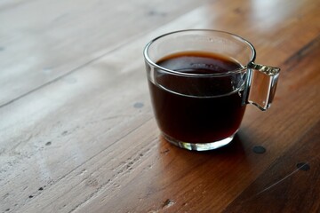 hot black coffee in transparent cup placed on wooden table in morning light.