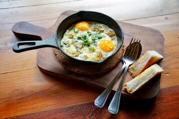 Pan Fried Egg with Toppings and bread slice on wooden tray. serve with spoon and fork. breakfast set in morning, hotel service.