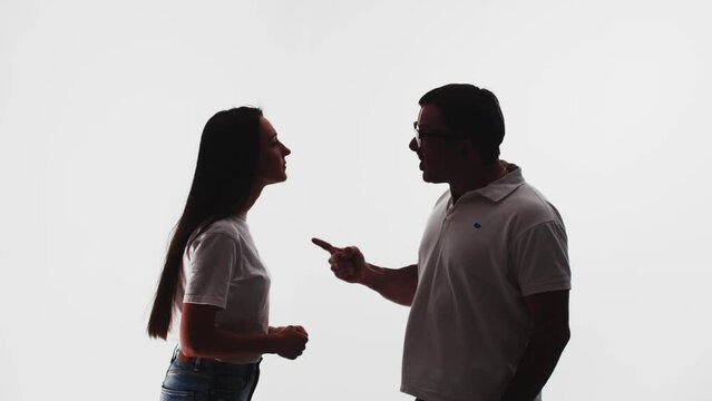 Silhouette of man screams and swears at woman, poke with finger, white background in studio. Man swears and gets angry at woman. Concept of shouting
