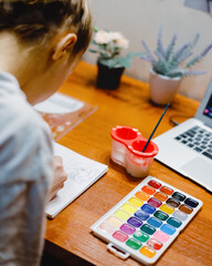 Young girl sits at table in her room and paints with watercolor paints. Theme of creativity,...