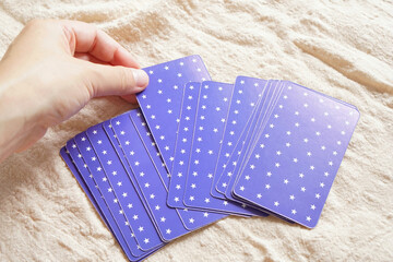 woman's hand choosing a purple tarot card from pile placed on linen fabric in the morning light. Reading fortune pass through pick a card by gypsy. Many type in arrange card to forecast destiny.