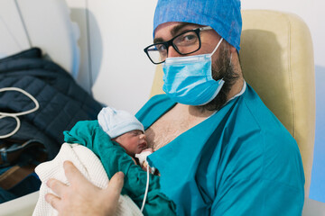 Man wearing face mask while holding his newborn baby in hospital room.